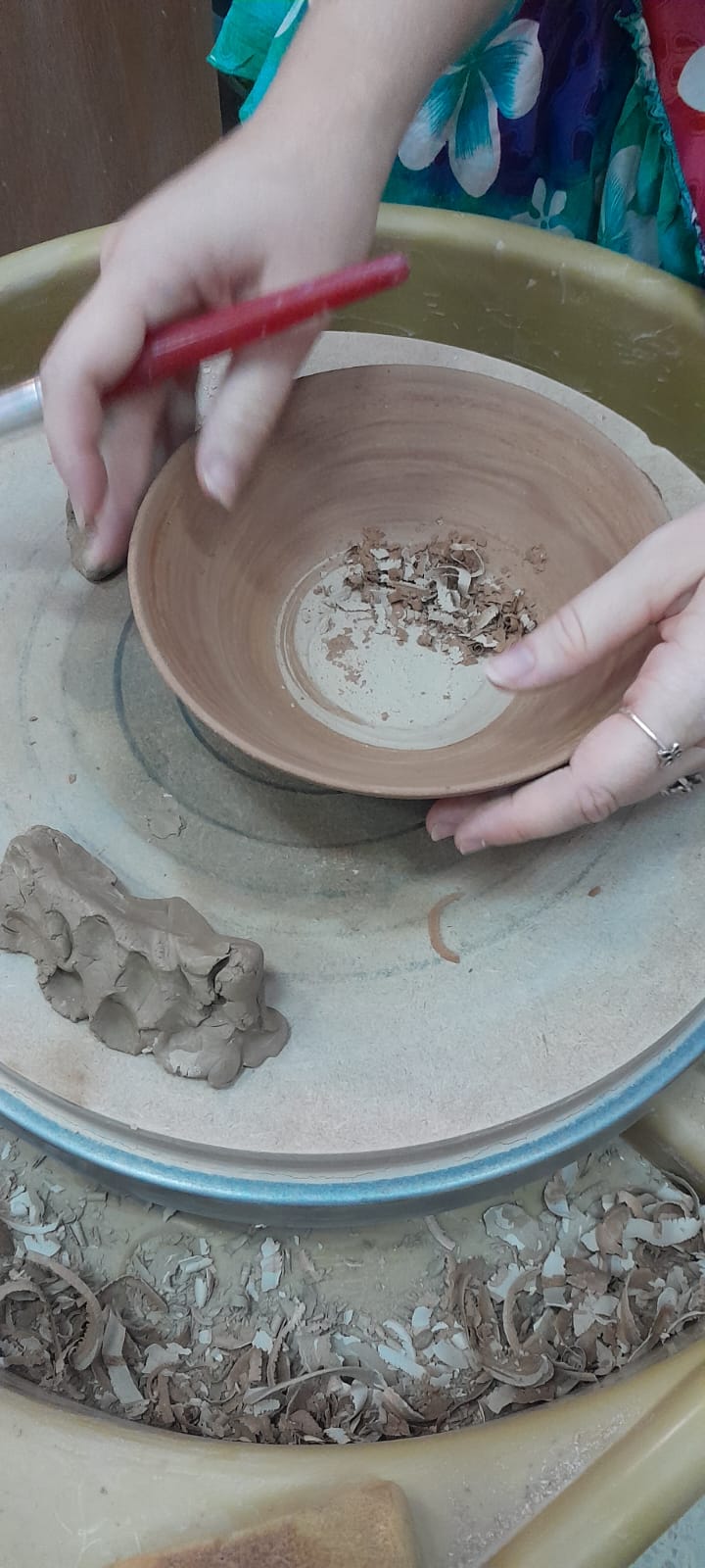 אישה מנקה קערת חרס על אובניים בעזרת כלי ייעודי