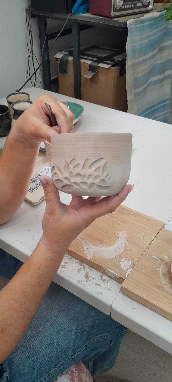 אישה מחזיקה כלי קרמיקה עם חריטת עלים עדינה