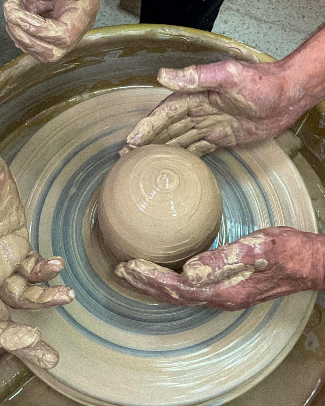 ידיים רבות מעצבות יחד כלי חימר על אובניים בתנועה סיבובית