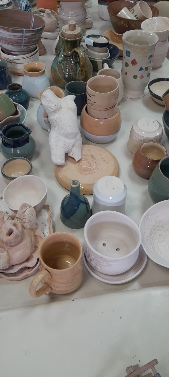 אוסף כלי קרמיקה על שולחן, כולל פסל טורסו נשי